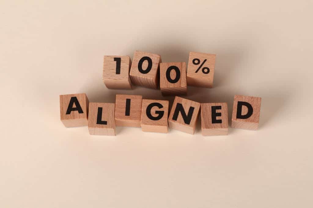 Wooden blocks spelling '100% Aligned' on a neutral background, conveying precision and alignment.